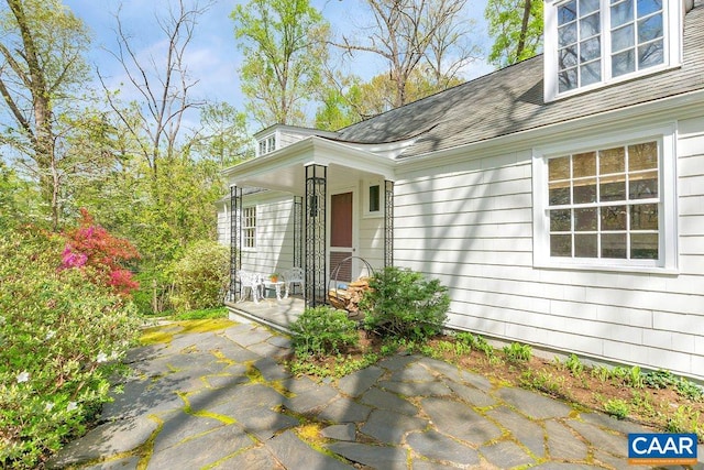 entrance to property featuring covered porch and a shingled roof