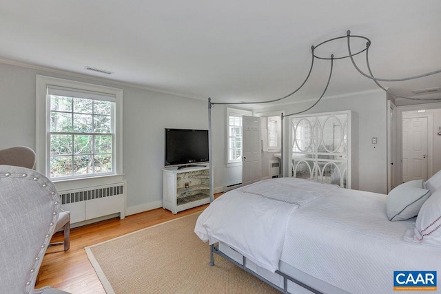 bedroom with radiator heating unit, crown molding, wood finished floors, multiple windows, and baseboards
