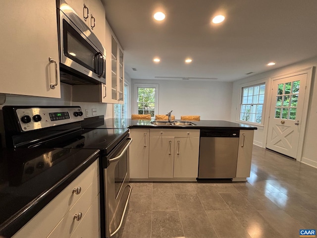 kitchen featuring appliances with stainless steel finishes, a sink, a peninsula, dark countertops, and recessed lighting