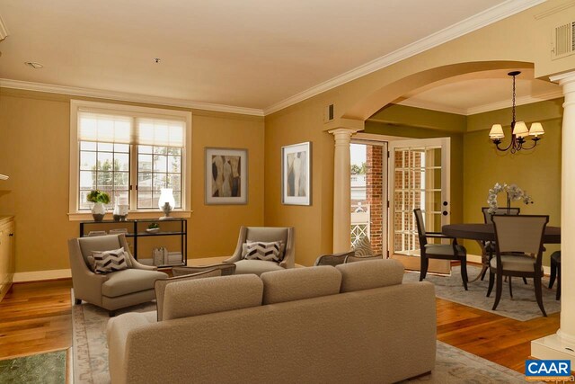 living area with arched walkways, decorative columns, wood finished floors, crown molding, and a chandelier