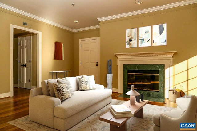 living area with wood finished floors, a premium fireplace, crown molding, recessed lighting, and baseboards