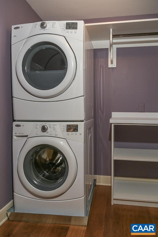 laundry room with stacked washing machine and dryer, wood finished floors, and baseboards