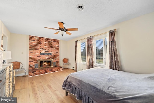  - bedroom featuring light wood finished floors, a brick fireplace, a baseboard heating unit, and a ceiling fan