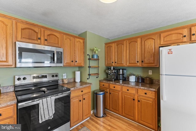 2266 Honeyville Rd, Stanley, VA 22851 - kitchen featuring stainless steel appliances, light wood-type flooring, brown cabinetry, and a textured ceiling