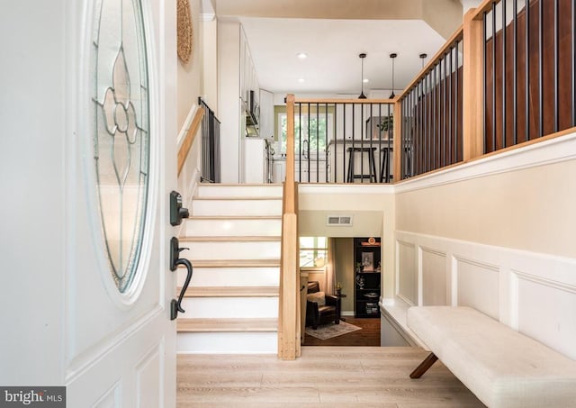  - foyer entrance with wood finished floors, a decorative wall, wainscoting, and stairway