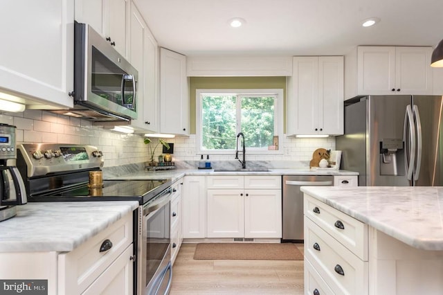 - kitchen featuring appliances with stainless steel finishes, white cabinets, light stone countertops, light wood-style floors, and recessed lighting