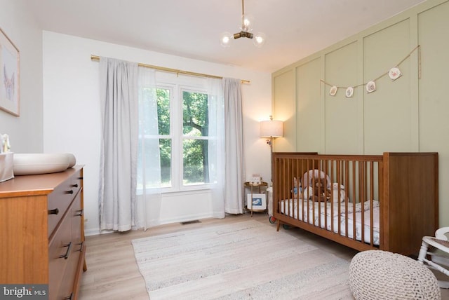  - bedroom featuring light wood-style flooring, a nursery area, and a chandelier