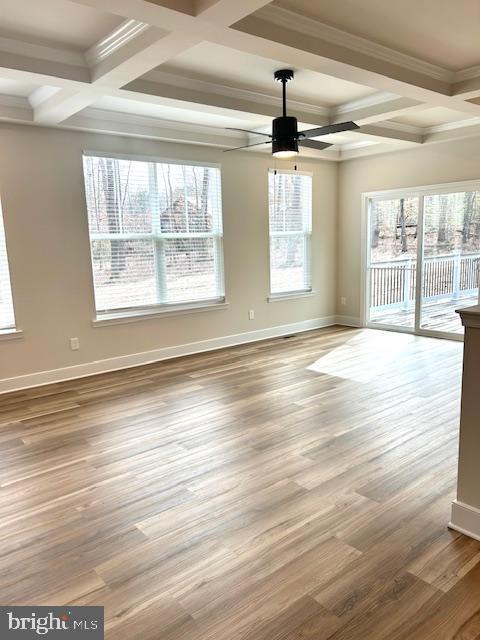empty room with coffered ceiling, ceiling fan, beam ceiling, baseboards, and wood finished floors