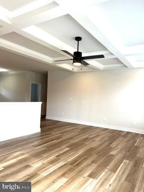 spare room with coffered ceiling, wood finished floors, a ceiling fan, baseboards, and beamed ceiling