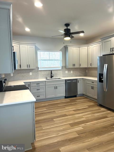 kitchen featuring appliances with stainless steel finishes, a sink, a ceiling fan, backsplash, and light wood finished floors