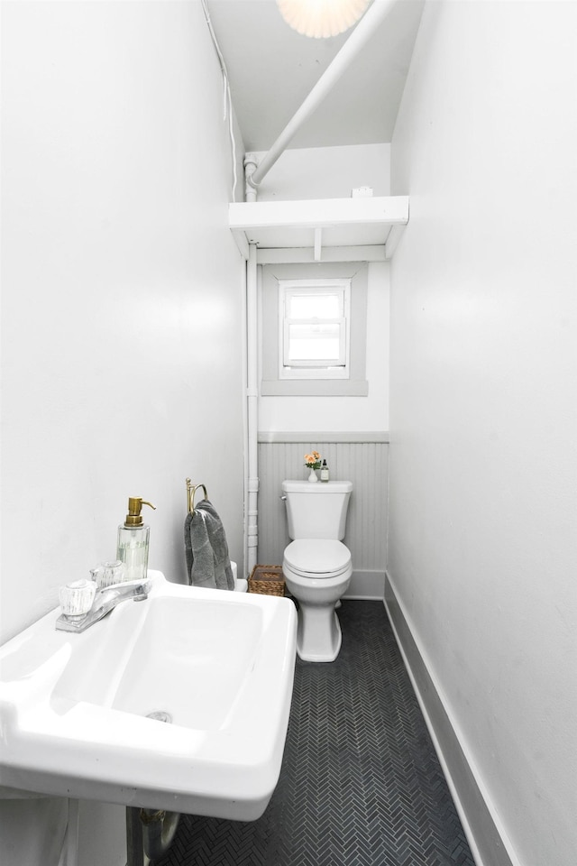 bathroom with a sink, toilet, baseboards, and a wainscoted wall