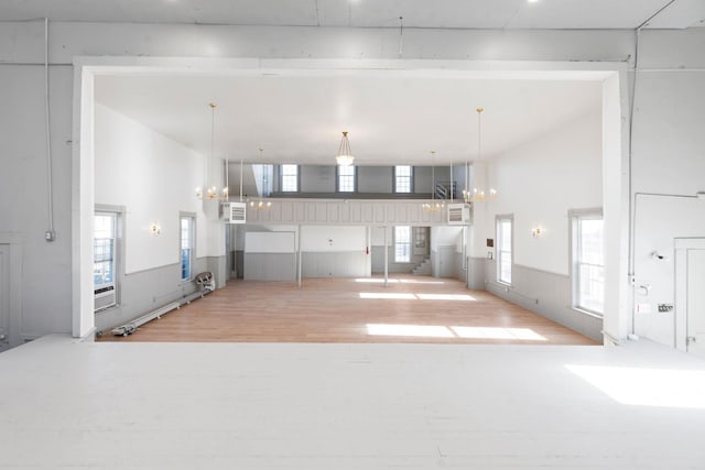 unfurnished living room with a wainscoted wall, an inviting chandelier, a wall unit AC, and wood finished floors