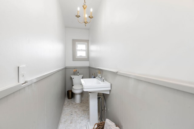 half bath with a wainscoted wall, toilet, and a chandelier