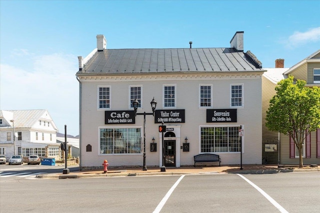view of front facade featuring a chimney, metal roof, a standing seam roof, and brick siding