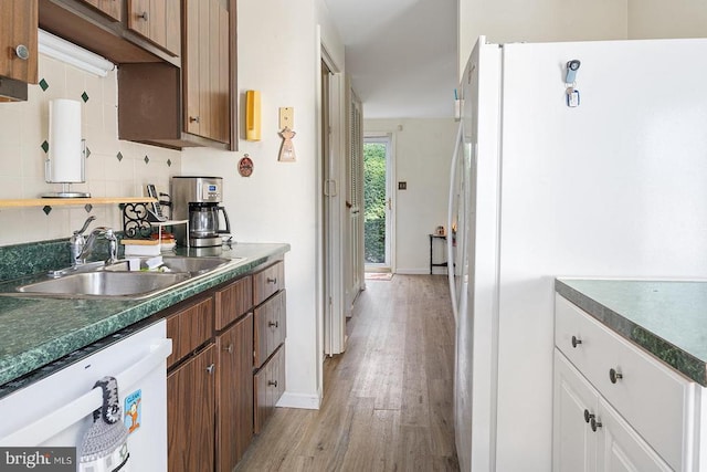  - kitchen featuring a sink, white appliances, light wood finished floors, dark countertops, and baseboards