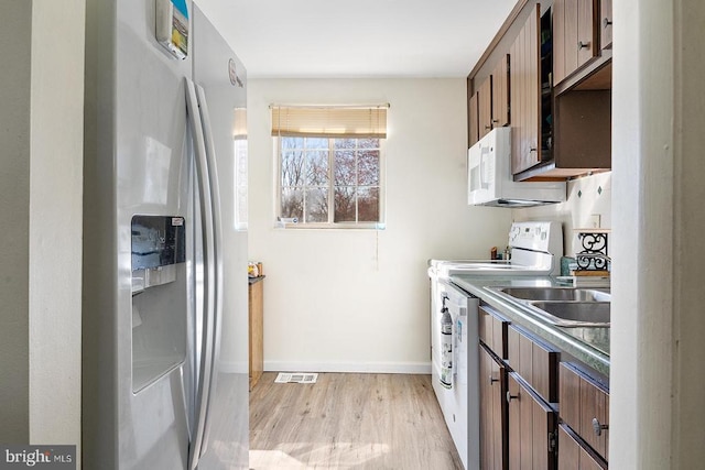  - kitchen featuring fridge with ice dispenser, white microwave, light wood-type flooring, baseboards, and a sink
