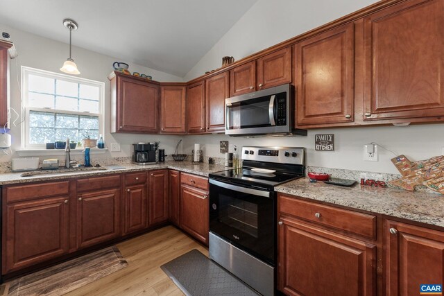 kitchen with a sink, stainless steel appliances, vaulted ceiling, hanging light fixtures, and light wood-style floors