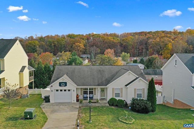 single story home with a garage, fence, concrete driveway, a front yard, and a forest view