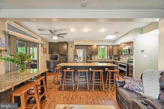 kitchen with stainless steel appliances, wood finished floors, open floor plan, a breakfast bar, and plenty of natural light