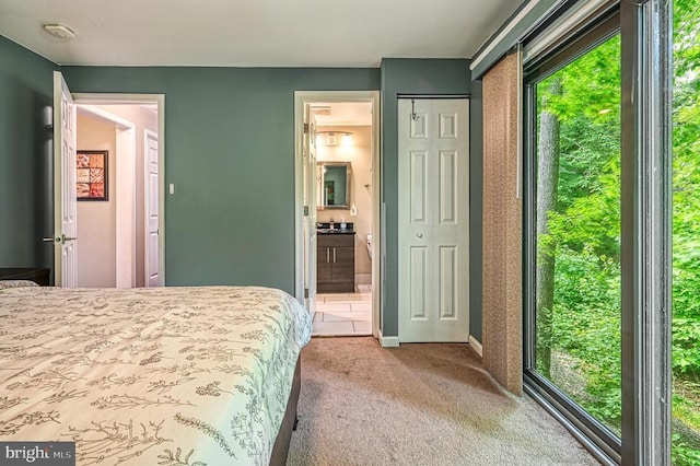 bedroom with multiple windows, light colored carpet, ensuite bathroom, and baseboards