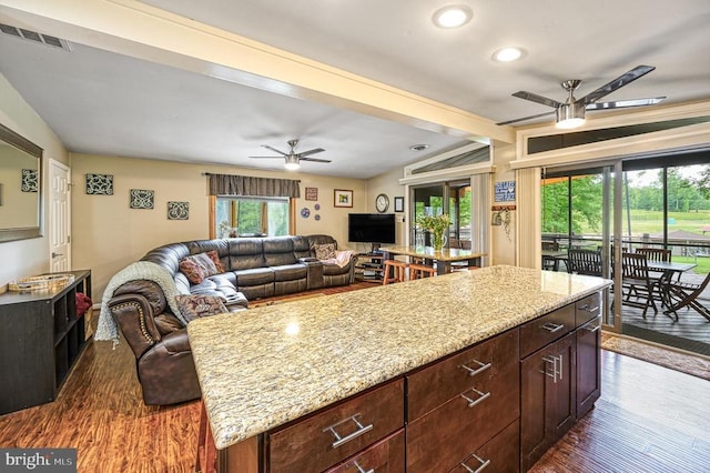 kitchen featuring a ceiling fan, a center island, dark wood finished floors, light stone countertops, and recessed lighting