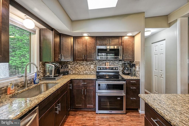 kitchen with appliances with stainless steel finishes, a sink, light stone countertops, backsplash, and dark wood-style flooring