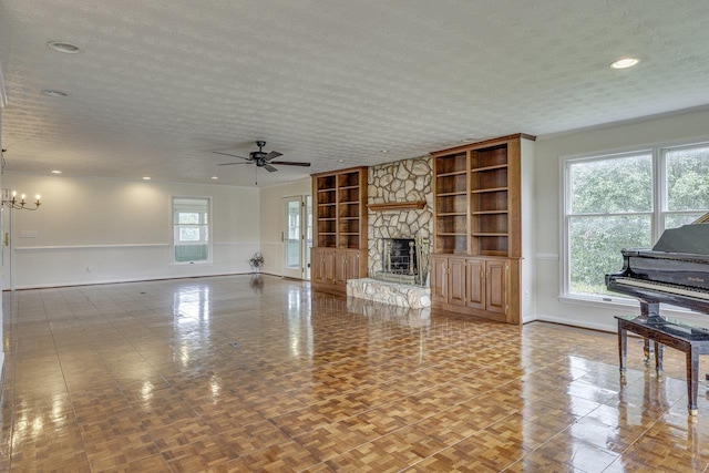 unfurnished living room featuring a textured ceiling, baseboards, built in features, ceiling fan with notable chandelier, and a fireplace