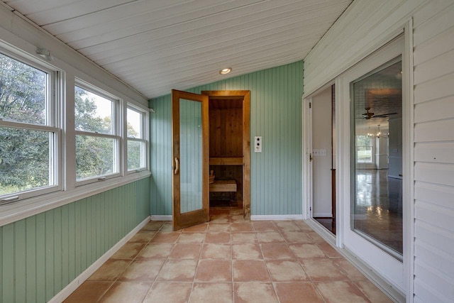 unfurnished sunroom featuring vaulted ceiling, wooden walls, and baseboards