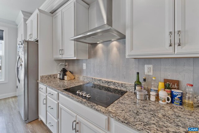 kitchen with wall chimney exhaust hood, black electric cooktop, freestanding refrigerator, white cabinets, and crown molding