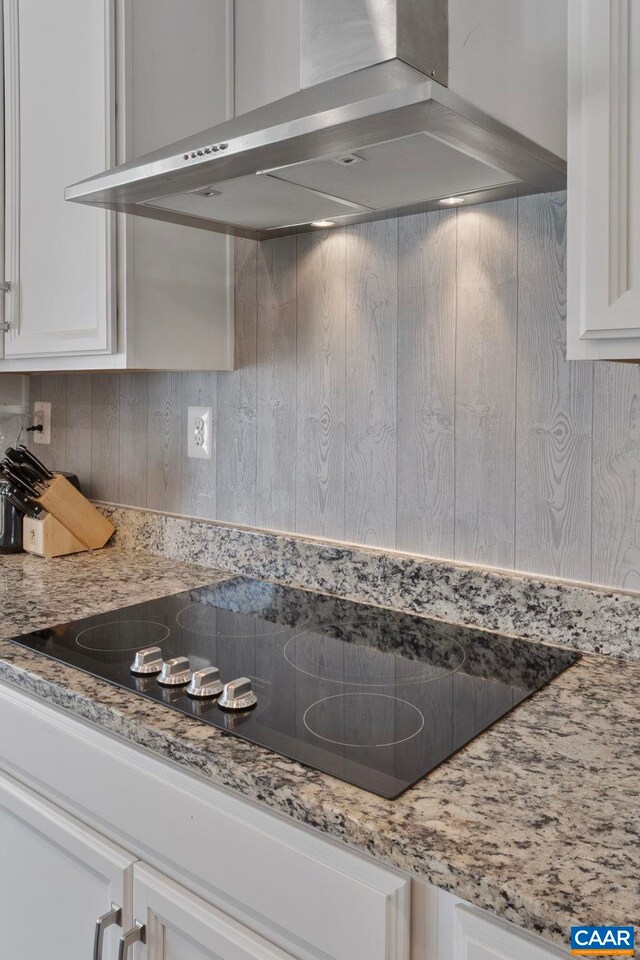 kitchen featuring wall chimney exhaust hood, white cabinetry, black electric stovetop, and light stone countertops