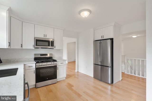 kitchen featuring stainless steel appliances, light wood-style floors, a sink, and white cabinets