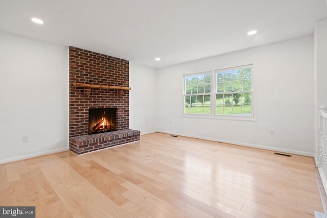 unfurnished living room with wood finished floors, a brick fireplace, baseboards, and recessed lighting