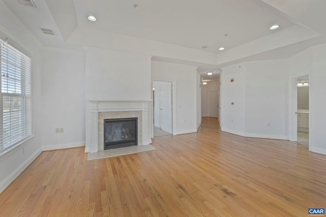 unfurnished living room with visible vents, light wood-style flooring, a raised ceiling, baseboards, and a fireplace with flush hearth