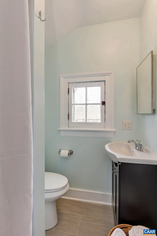 bathroom with lofted ceiling, toilet, baseboards, tile patterned floors, and vanity