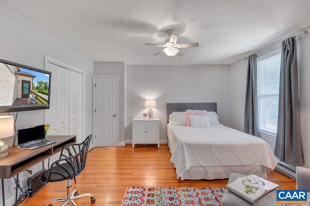 bedroom with a baseboard heating unit, a closet, a ceiling fan, and wood finished floors