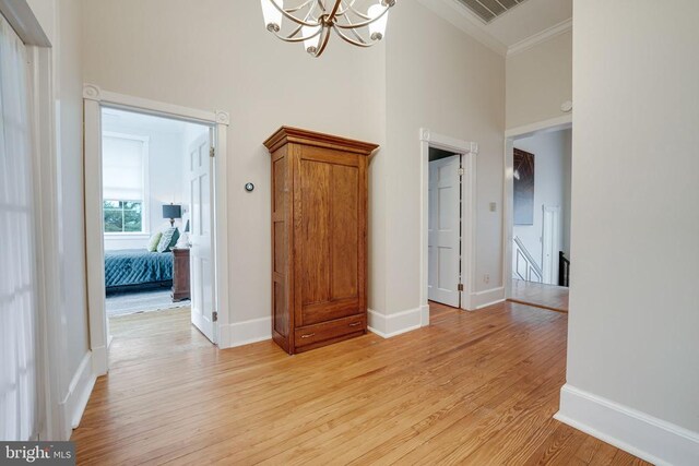  - unfurnished room with crown molding, light wood-style flooring, a high ceiling, and a chandelier