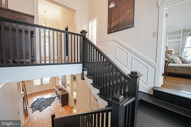  - stairs featuring wood finished floors, a chandelier, wainscoting, and a decorative wall