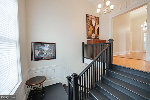  - staircase with a chandelier, wood finished floors, and wainscoting
