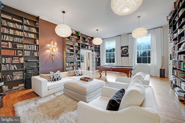  - living area with wall of books, wood finished floors, pool table, and built in shelves