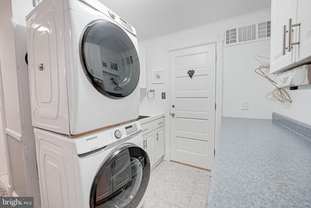  - washroom with stacked washer and clothes dryer, cabinet space, light tile patterned flooring, and ornamental molding