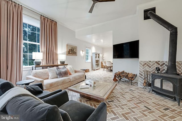  - living room featuring a wood stove, brick patterned flooring, ornamental molding, and a ceiling fan