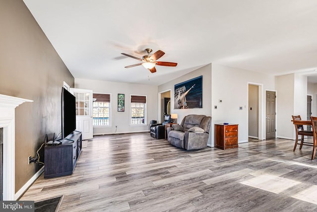 living area featuring a ceiling fan, wood finished floors, baseboards, and a fireplace