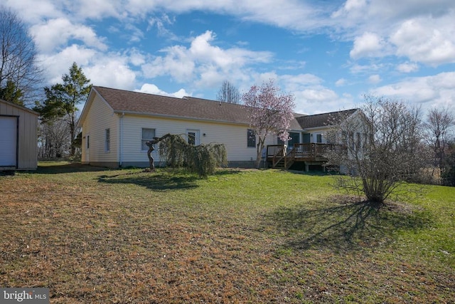  - back of property featuring a wooden deck, a lawn, and an outbuilding
