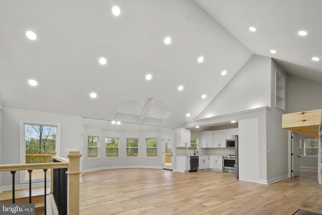 unfurnished living room featuring high vaulted ceiling, light wood finished floors, baseboards, recessed lighting, and a sink