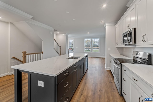 kitchen featuring a sink, stainless steel appliances, white cabinets, a kitchen island with sink, and ornamental molding