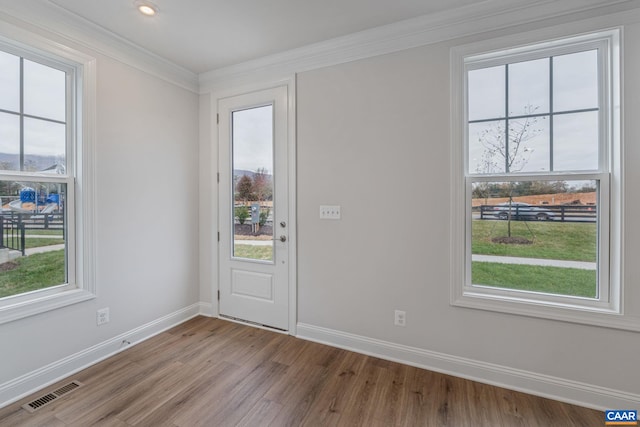 doorway with light wood finished floors, visible vents, baseboards, and ornamental molding