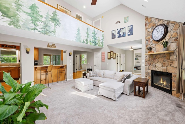 living room featuring ceiling fan, high vaulted ceiling, light carpet, a fireplace, and baseboards