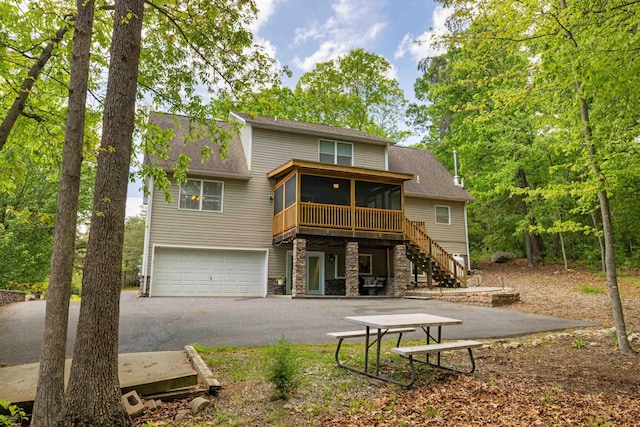 back of property featuring a sunroom, stone siding, stairway, an attached garage, and asphalt driveway