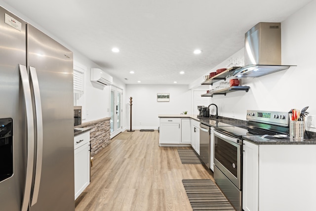 kitchen with appliances with stainless steel finishes, range hood, a wall mounted AC, white cabinetry, and light wood-style flooring