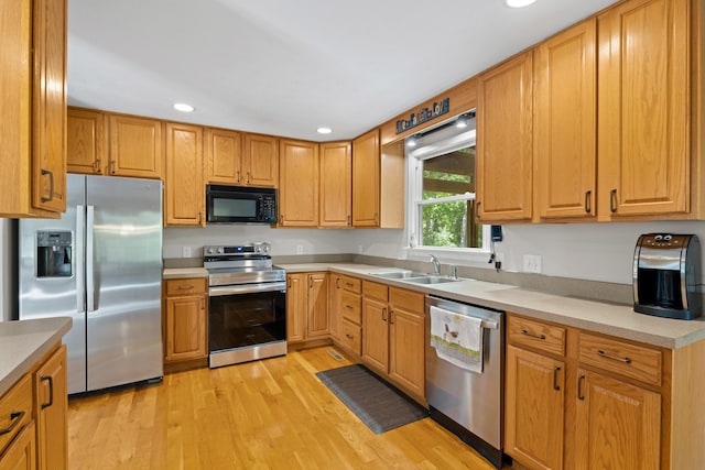 kitchen featuring appliances with stainless steel finishes, a sink, recessed lighting, light wood-style floors, and light countertops
